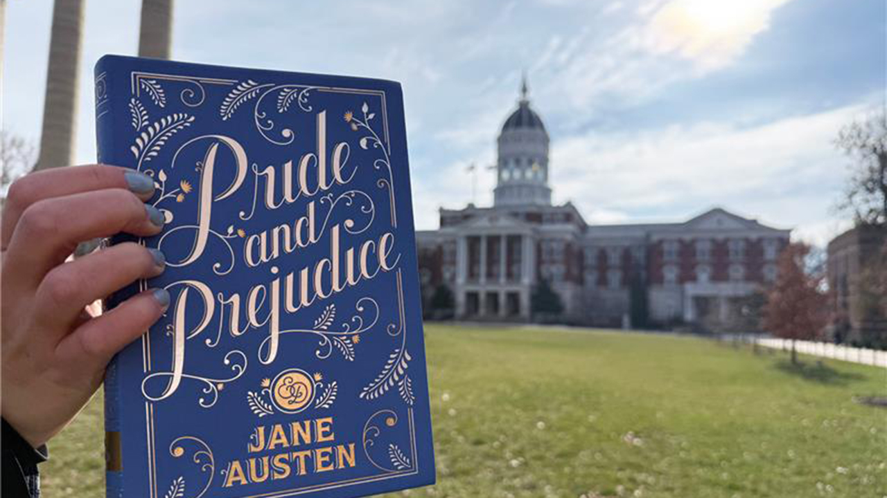 Hand holding Pride and Prejudice with Jesse Hall in background