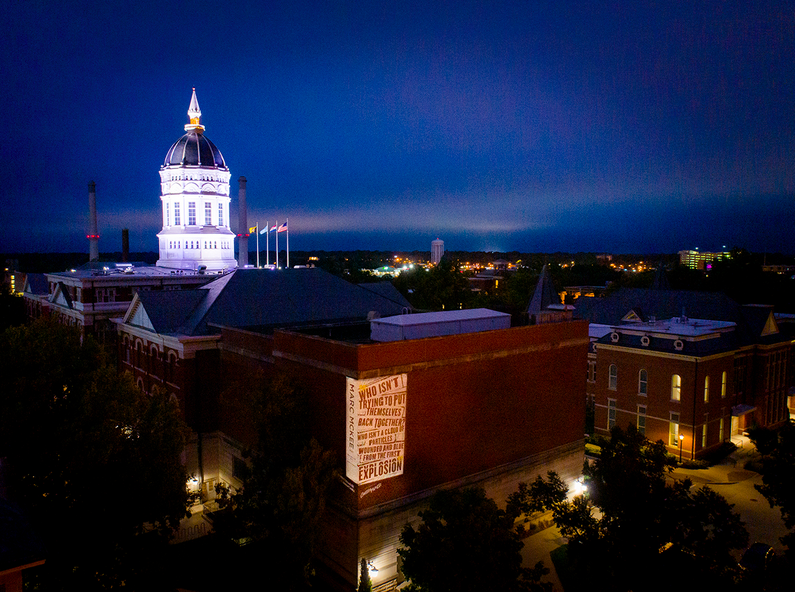 Aerial photo of projected poetry and illuminated Jesse Hall dome at night.